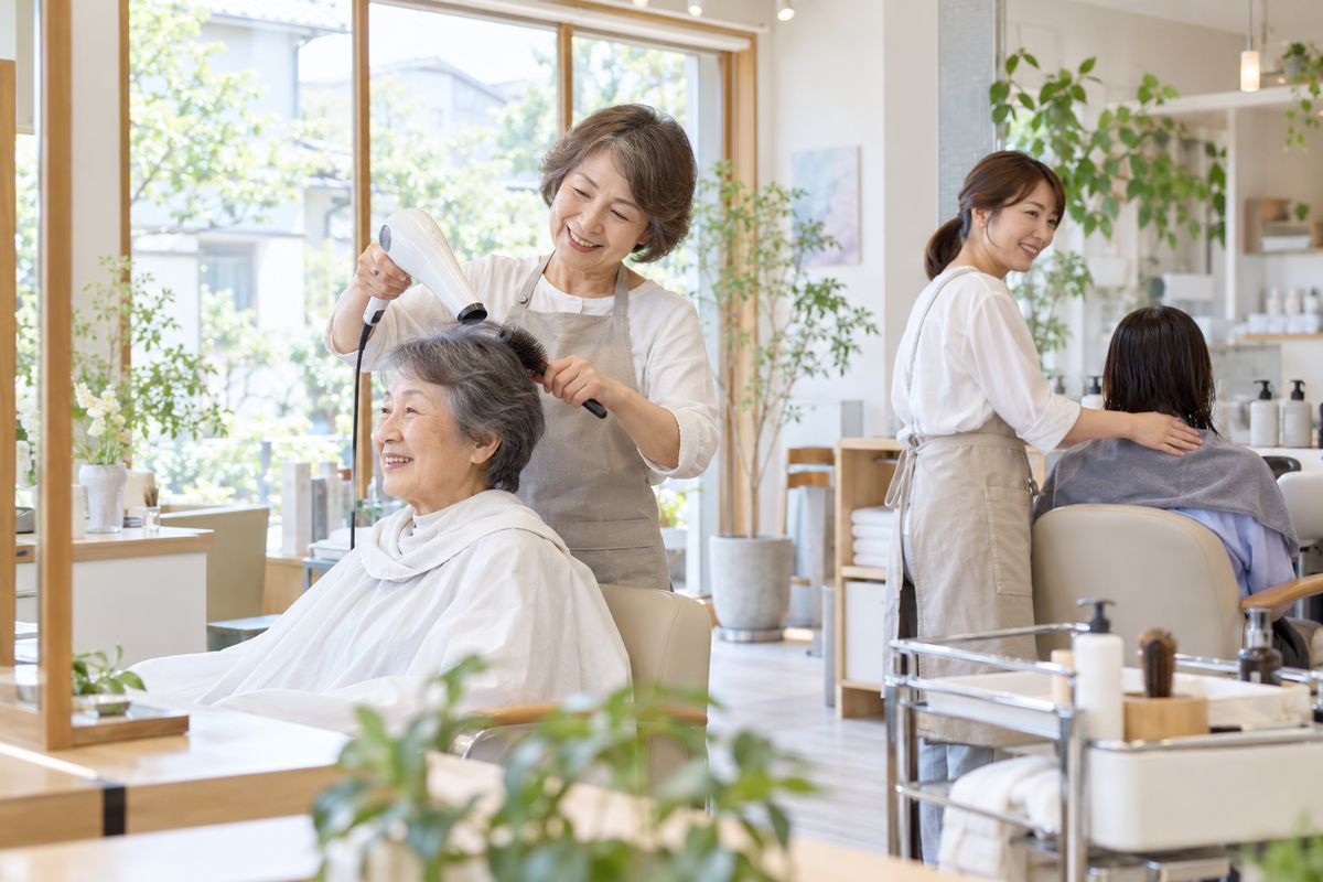 住宅街の美容室で、世代の違うスタッフが中高年のお客様を担当するイメージ