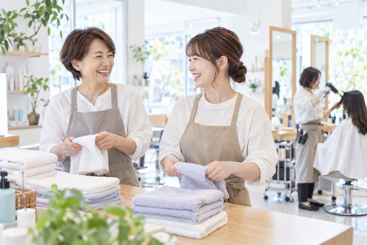 世代の違うスタッフが笑顔でタオルをたたむ美容室のイメージ